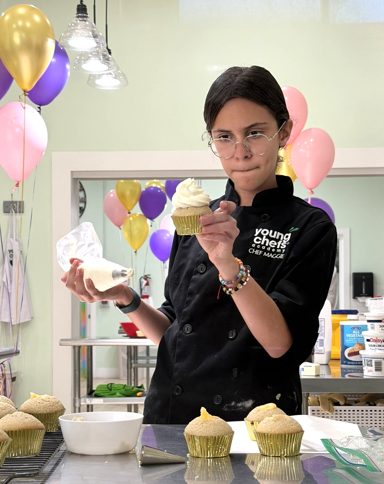Maggie in her chef coat piping frosting onto a freshly baked cupcake